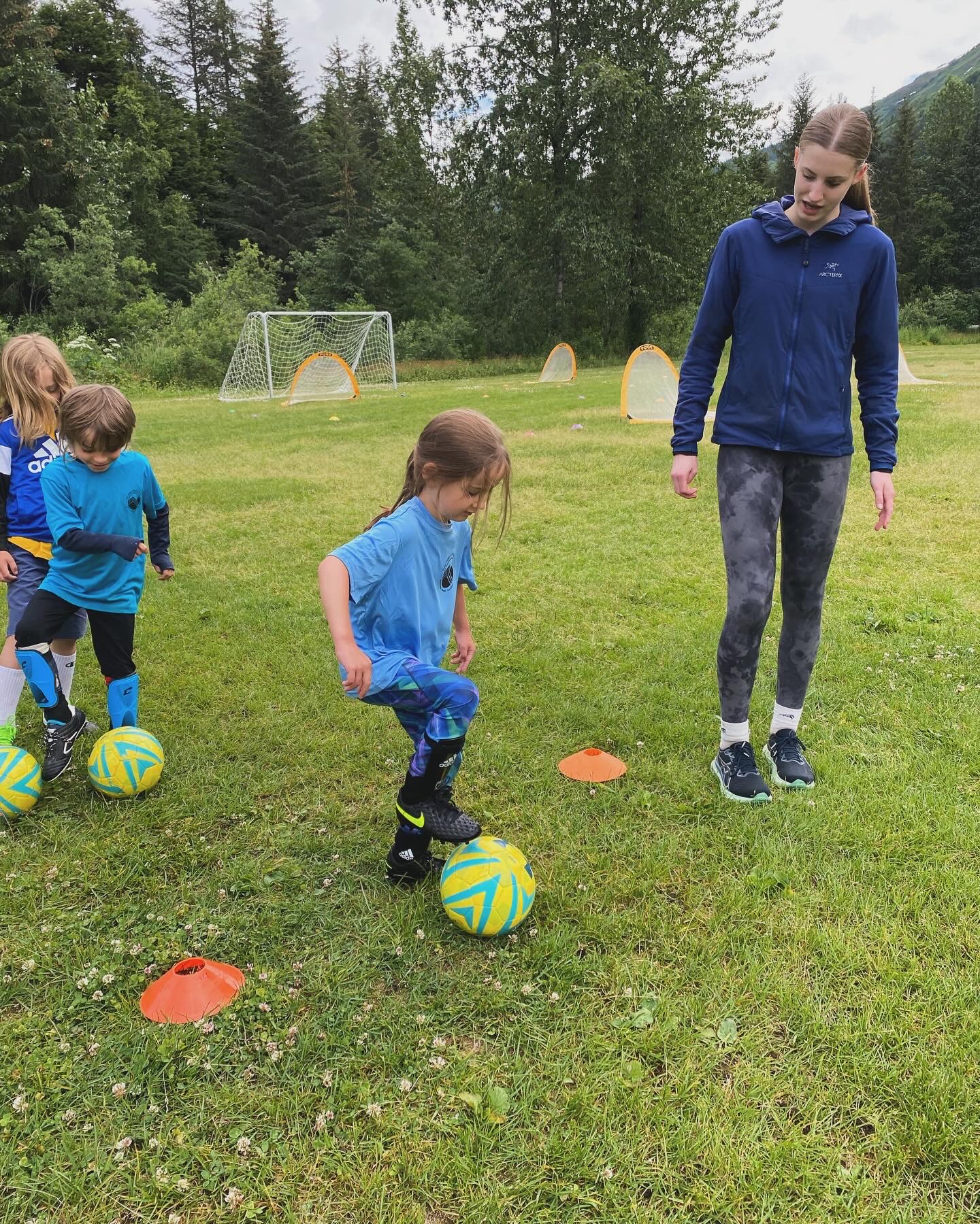 Children doing soccer ball drills with coach on field